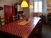 Eine gewölbte alte Küche. In der Mitte steht ein grosser Tisch mit zehn Stühlen darum. Der Tisch ist von einem roten Wachstuch mit weissen Punkten bedeckt.