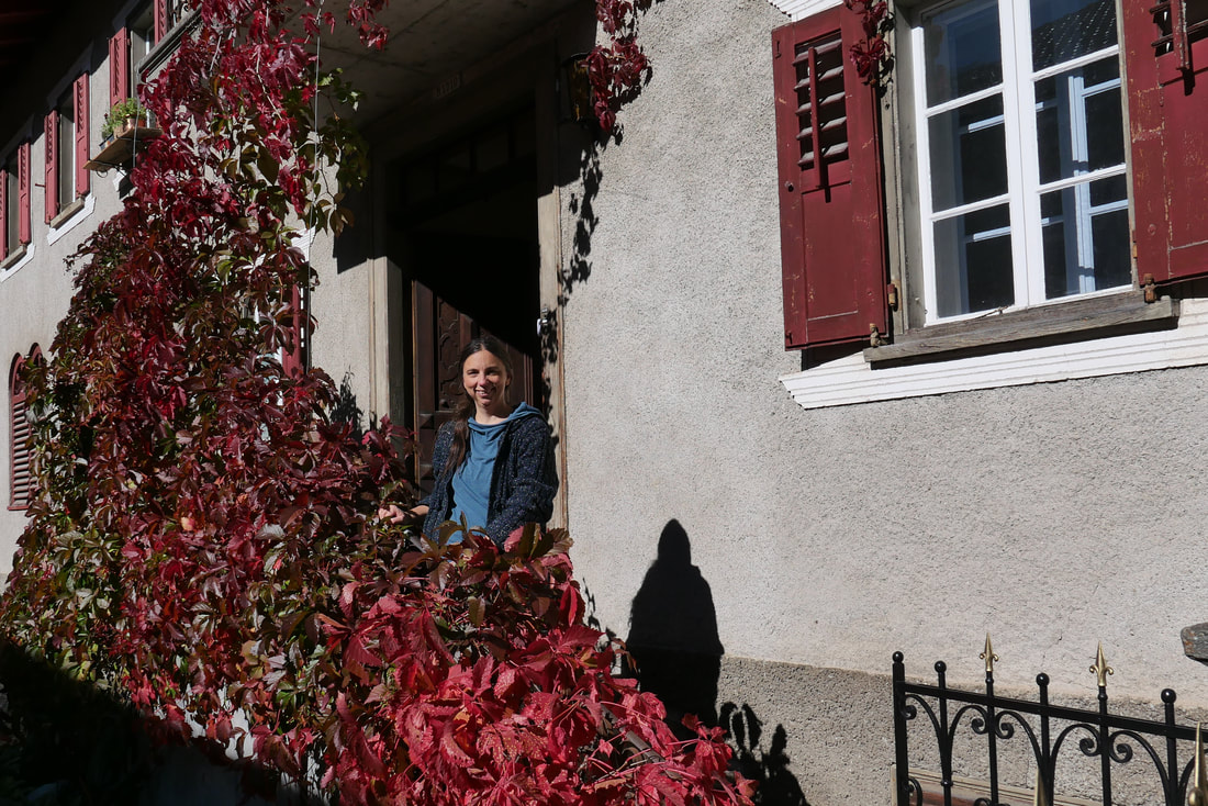 Eine Frau steht vor einer offenen Haustür und lächelt.